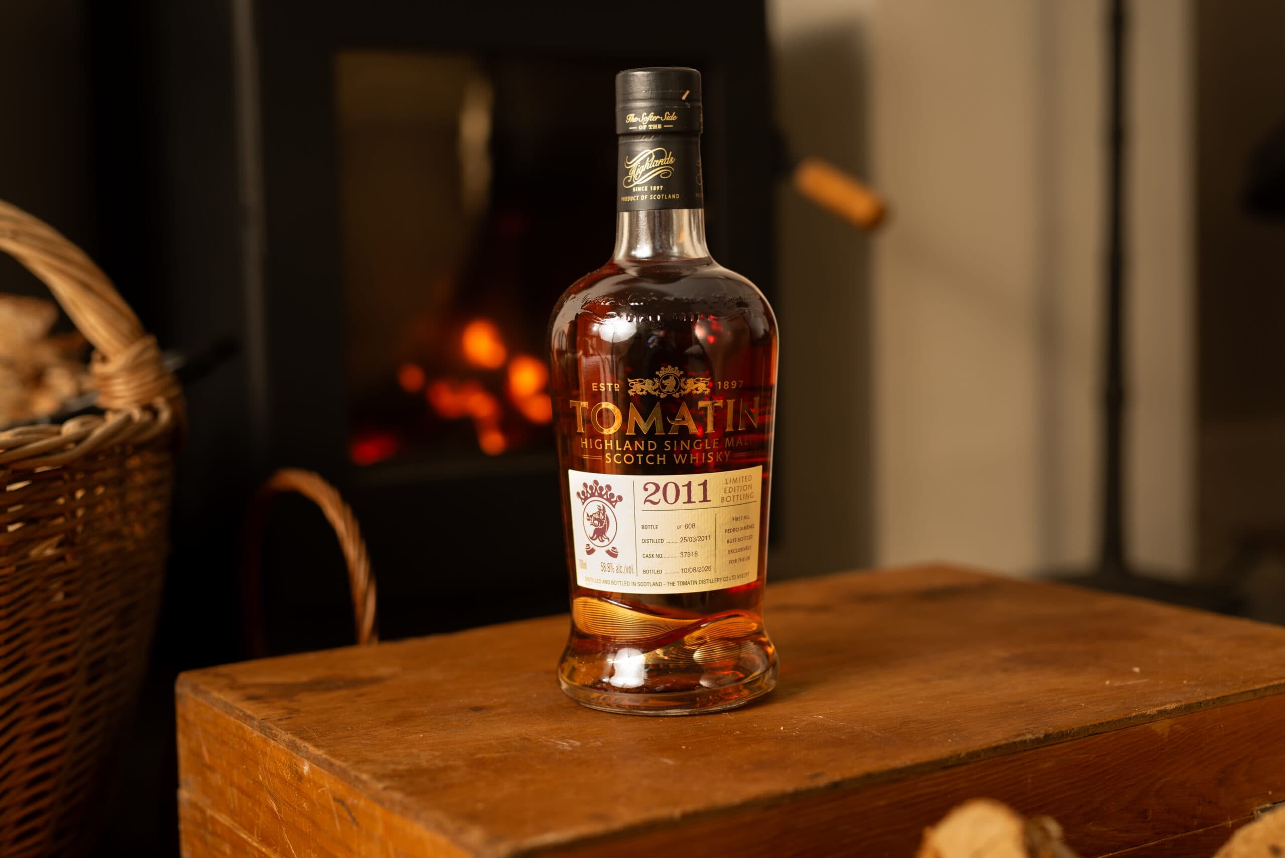 A bottle of Tomatin 2011 Single Cask on a wooden box beside a fire